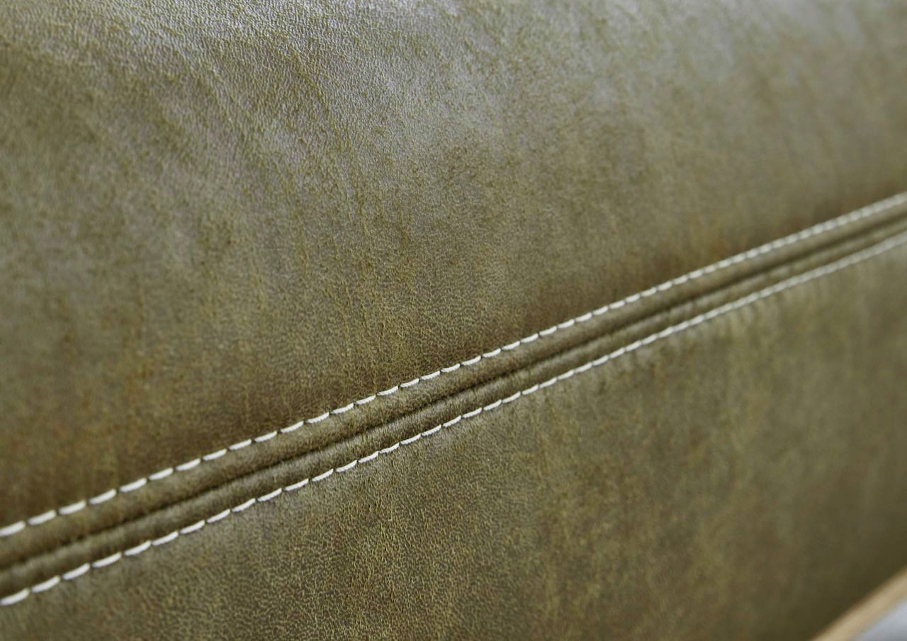 Nahaufnahme einer olivgrünen Lederoberfläche mit weißen Ziernähten, seitliche Perspektive.