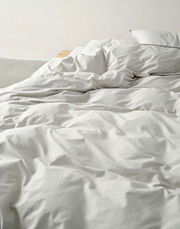 Nahaufnahme einer ungemachten Bettwäsche in Cremefarbe auf einem Bett.