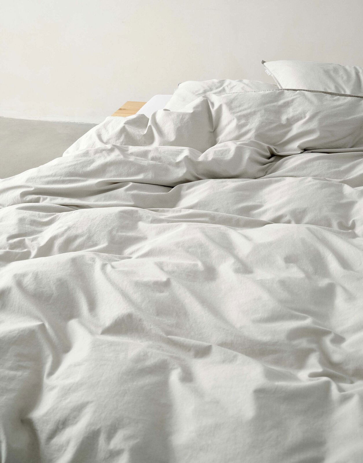 Nahaufnahme einer ungemachten Bettwäsche in Cremefarbe auf einem Bett.