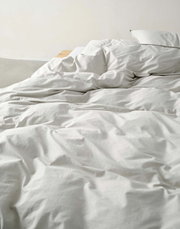 Nahaufnahme einer ungemachten Bettwäsche in Cremefarbe auf einem Bett.