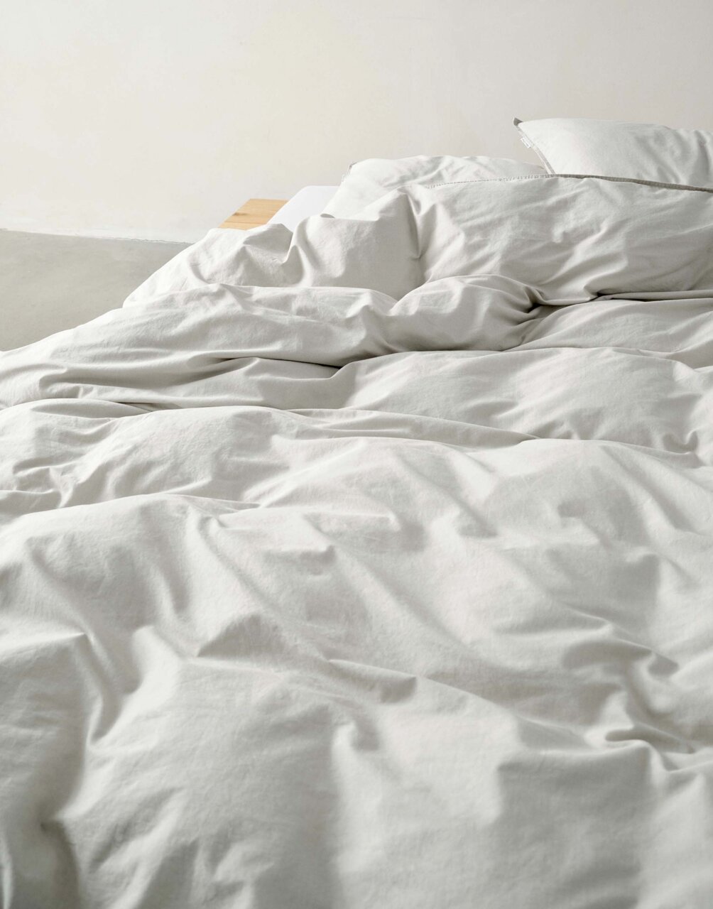 Nahaufnahme einer ungemachten Bettwäsche in Cremefarbe auf einem Bett.