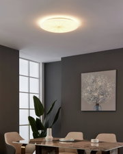 LED-Deckenleuchte NIEVES 1 in einem modernen Wohnzimmer, von unten betrachtet, mit sanftem, warmem Licht, das den Raum beleuchtet.