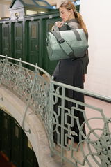 Frau trägt eine grüne Tasche über der Schulter auf einem Balkon mit dekorativem Geländer, seitliche Perspektive