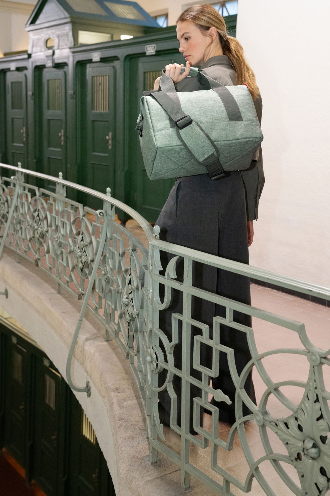 Frau trägt eine grüne Tasche über der Schulter auf einem Balkon mit dekorativem Geländer, seitliche Perspektive