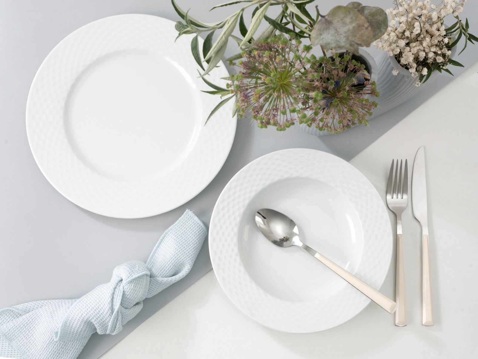 Tafelservice 12-tlg mit weißem Teller und Schüssel, Besteck und Blumenarrangement aus der Vogelperspektive