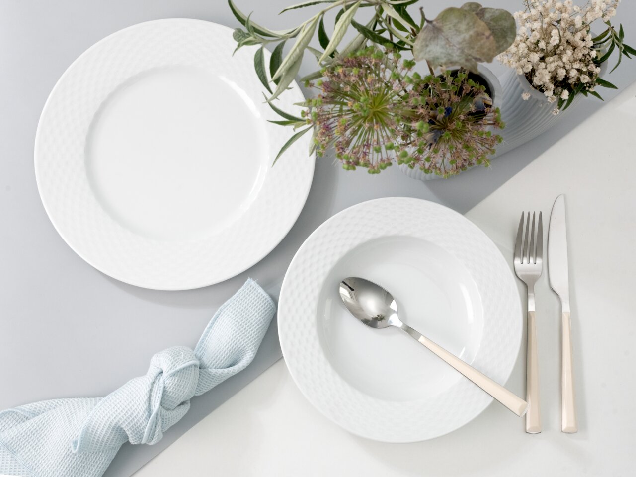 Tafelservice 12-tlg mit weißem Teller und Schüssel, Besteck und Blumenarrangement aus der Vogelperspektive