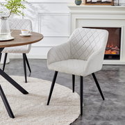 Gepolsterter Esszimmerstuhl in Hellbeige mit rautenförmiger Steppung und schwarzen Metallbeinen, in schräger Frontansicht neben einem runden Holztisch vor einem Kamin.