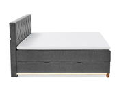 Seitenansicht eines grauen Boxspringbetts mit gestepptem Kopfteil und weißer Matratze.