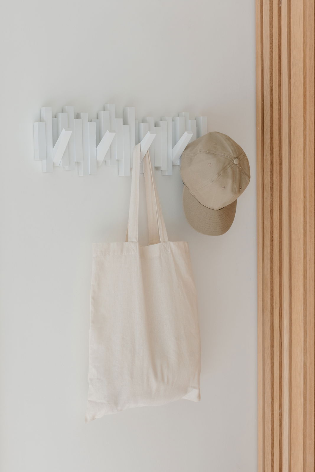 Moderne weiße Wandgarderobe mit mehreren Haken, an der eine beige Tasche und eine Kappe hängen, aus der Frontalperspektive fotografiert.