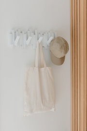 Moderne weiße Wandgarderobe mit mehreren Haken, an der eine beige Tasche und eine Kappe hängen, aus der Frontalperspektive fotografiert.