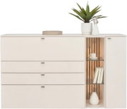 Witte moderne dressoir/commode met vier laden links en open verlichte vitrinekast rechts met verticale houten latten en glazen planken, gefotografeerd in frontaal aanzicht; bovenop een plant in witte pot en decoratie.