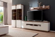 Modernes Wohnzimmer-Entertainment-Set in Weiß mit Holzoptik: TV-Lowboard mit Schubladen und offenen Fächern, zwei hohe Vitrinenschränke mit Glastüren und Wandregal über einem Fernseher, Frontansicht in leichter Schrägperspektive von links