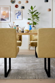 Zwei gelbe Stühle mit schwarzem Metallgestell, von hinten gesehen, vor einem Holztisch in einem modern dekorierten Raum.