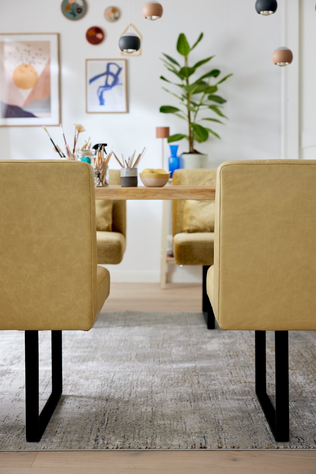 Zwei gelbe Stühle mit schwarzem Metallgestell, von hinten gesehen, vor einem Holztisch in einem modern dekorierten Raum.