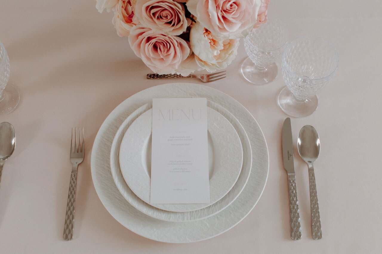 Elegante Tischdekoration mit Weißweingläsern, Blumenstrauß und Menükarten aus der Vogelperspektive.