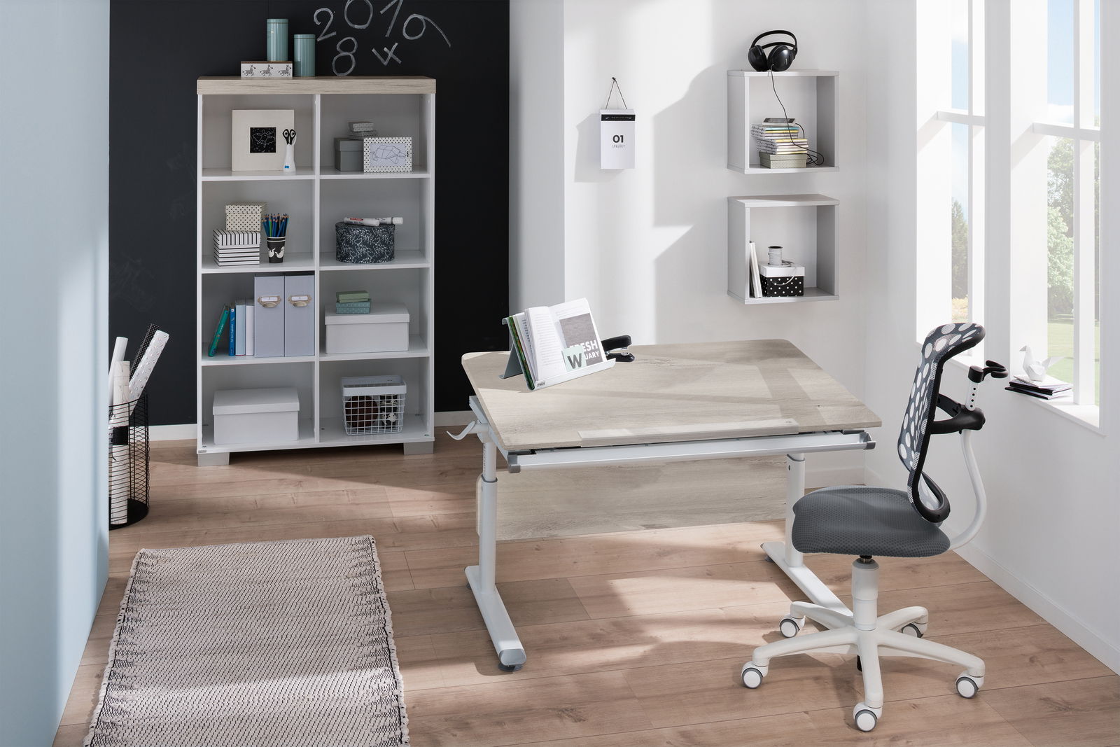 Moderner Schreibtisch in einem hellen Raum mit ergonomischem Stuhl, Bücherregal und Wandregalen, seitliche Perspektive.