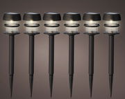 Sechs schwarze Solar-Stabbeleuchten aus Plastik in einer frontalen Ansicht, die gleichmäßig leuchten.