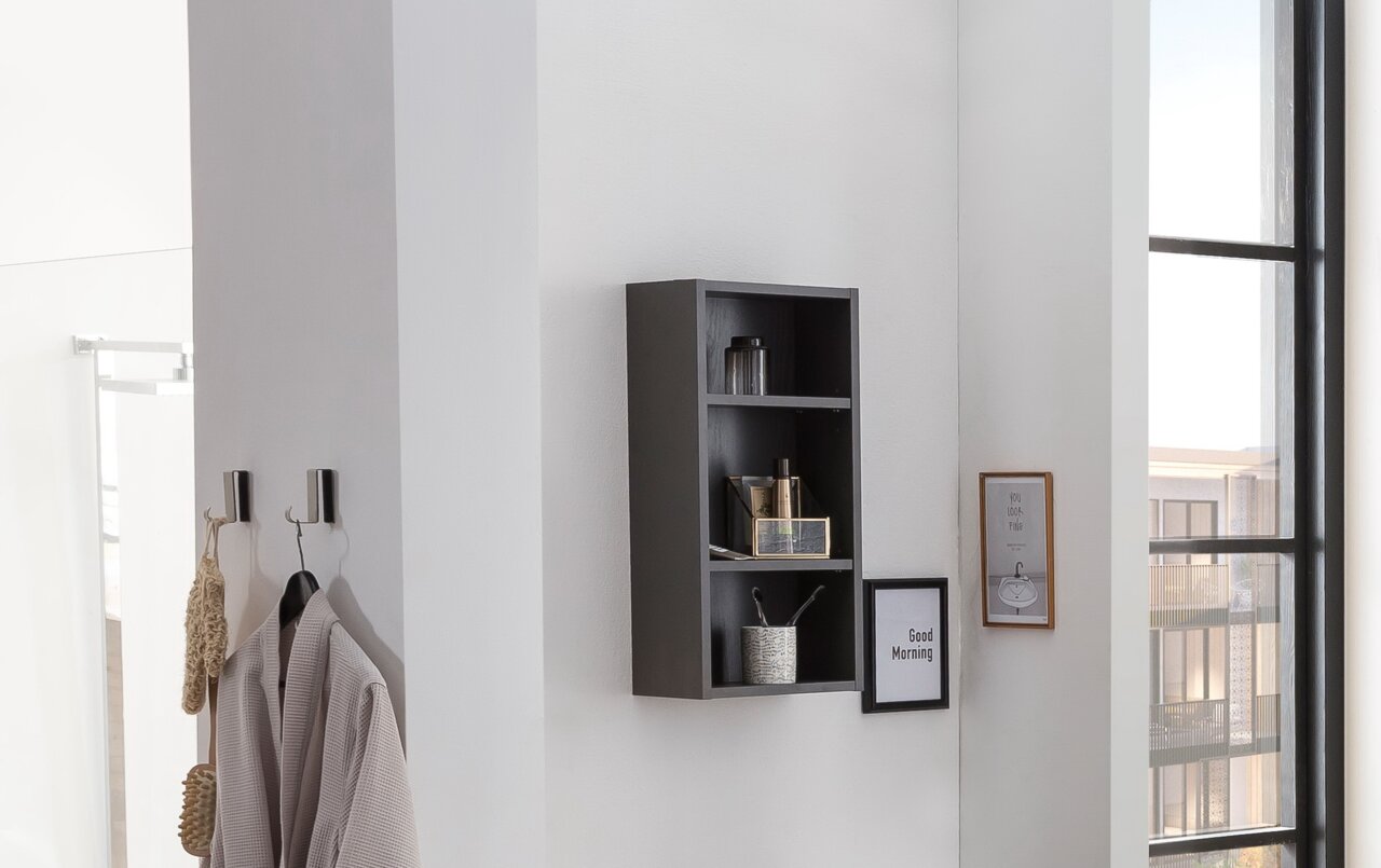 Schwarzes Hängeregal an einer weißen Wand, frontal fotografiert, mit mehreren Fächern, die dekorative Gegenstände und Pflegeprodukte enthalten.