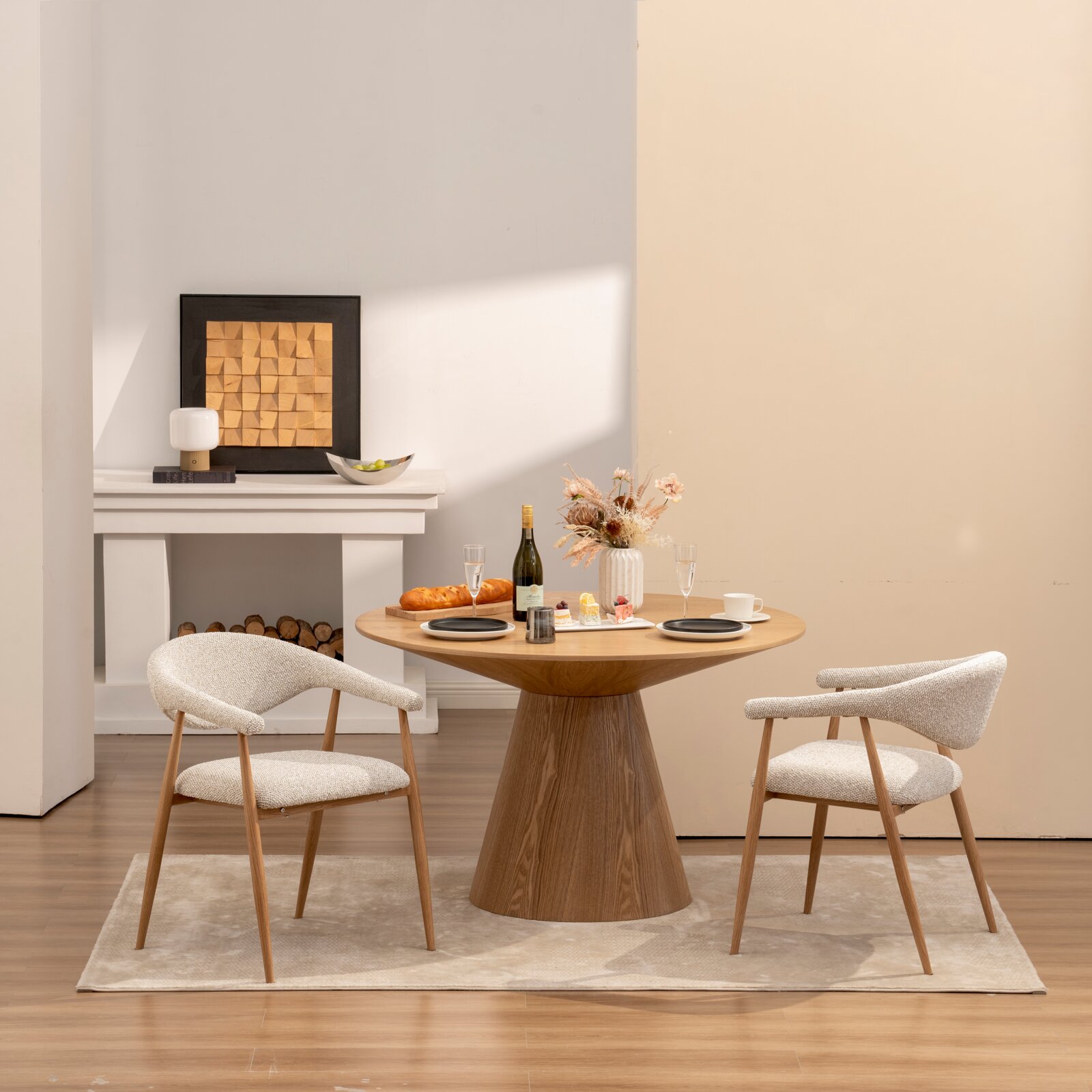 Modernes Esszimmer-Set mit rundem Holztisch und zwei gepolsterten Armlehnenstühlen in hellem Stoff, dekoriert mit Wein, Gebäck und Vase, fotografiert in frontaler leicht seitlicher Perspektive auf Augenhöhe.