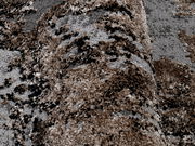 Nahaufnahme eines strukturierten Teppichs in Braun- und Grautönen, perspektivisch von der Seite aufgenommen.