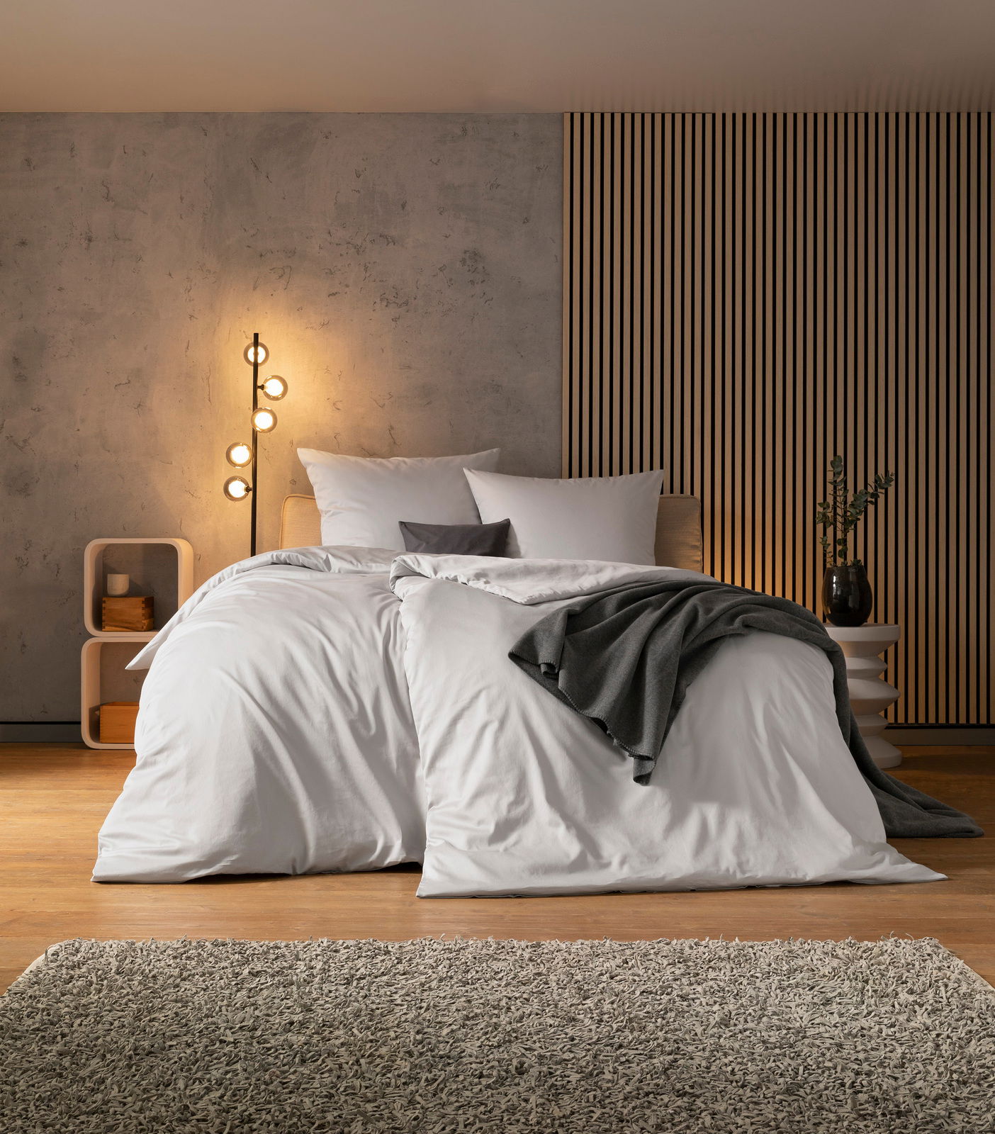 Gemütliches Schlafzimmer mit modernem Design, Bett mit weißer Bettwäsche und grauer Decke, seitliche Perspektive
