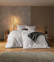 Gezellige slaapkamer met een modern ontwerp, bed met wit beddengoed en een grijze deken, zijaanzicht