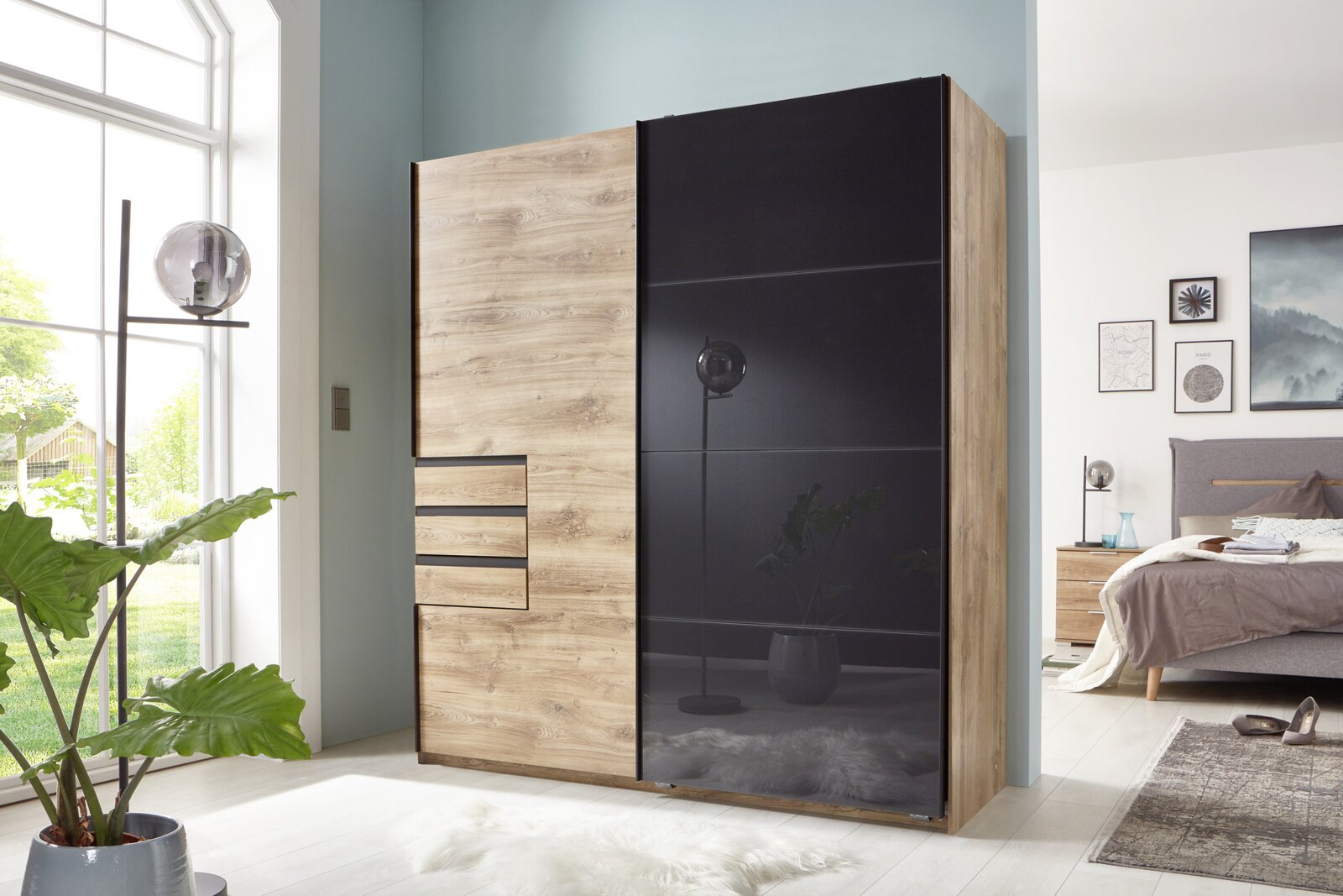 Schwebetürenschrank mit zwei Türen, links in Holzoptik und rechts in schwarzem Hochglanz, in einem modernen Schlafzimmer mit Blick aus der Ecke des Raumes.
