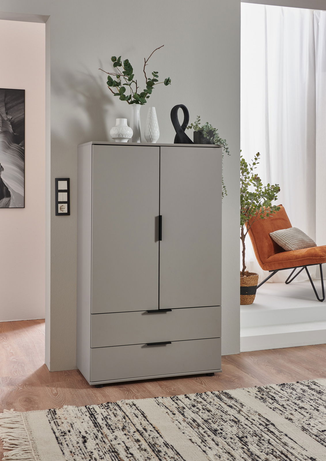 Graue Kommode mit zwei Türen und zwei Schubladen, dekoriert mit Vasen und Pflanzen, aus frontaler Perspektive fotografiert.