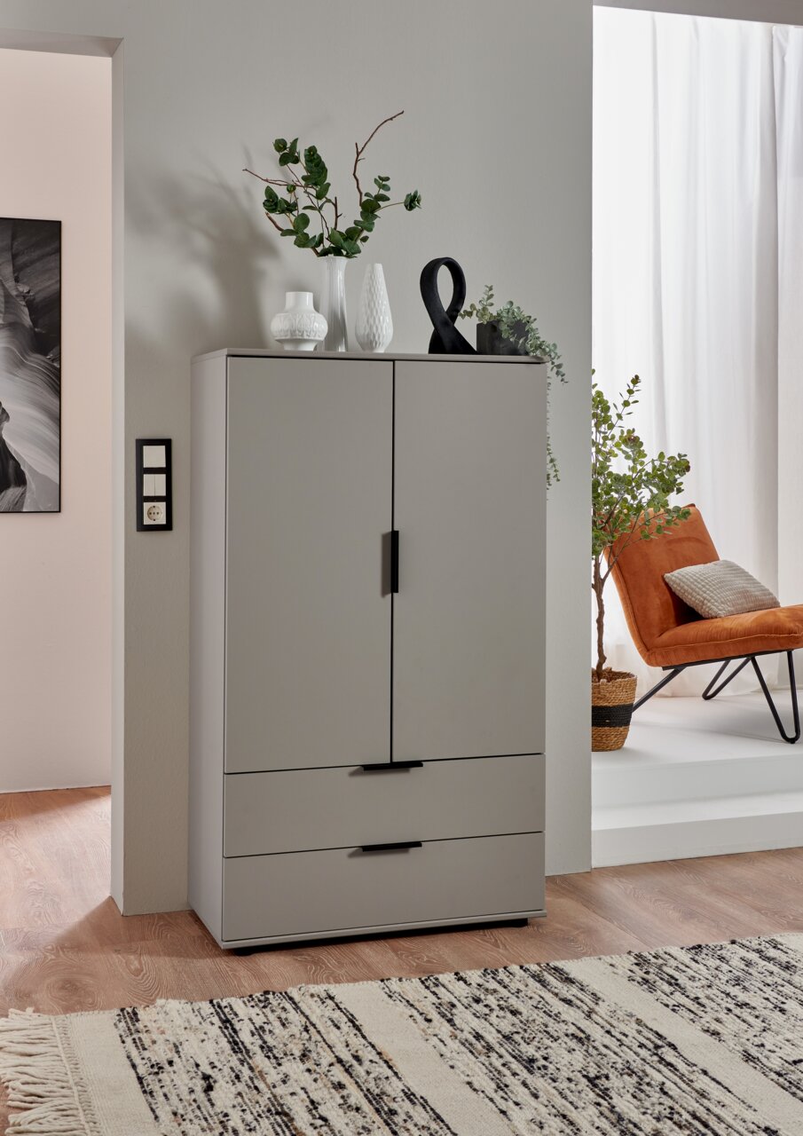 Graue Kommode mit zwei Türen und zwei Schubladen, dekoriert mit Vasen und Pflanzen, aus frontaler Perspektive fotografiert.