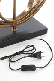 Nahaufnahme eines Lampenfußes mit einem goldenen Metallrahmen auf einem schwarzen Sockel, inklusive Kabel und Schalter, aus seitlicher Perspektive.