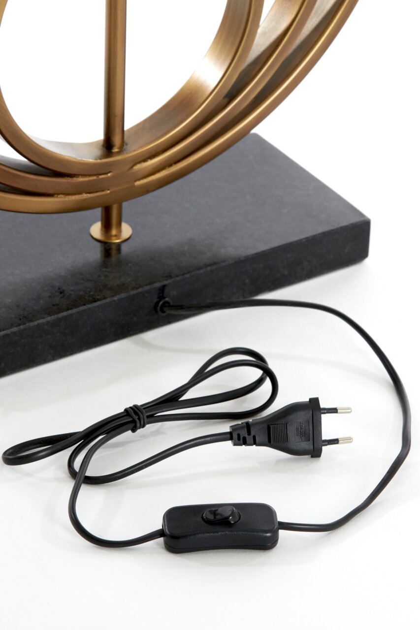 Nahaufnahme eines Lampenfußes mit einem goldenen Metallrahmen auf einem schwarzen Sockel, inklusive Kabel und Schalter, aus seitlicher Perspektive.