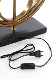 Nahaufnahme eines Lampenfußes mit einem goldenen Metallrahmen auf einem schwarzen Sockel, inklusive Kabel und Schalter, aus seitlicher Perspektive.