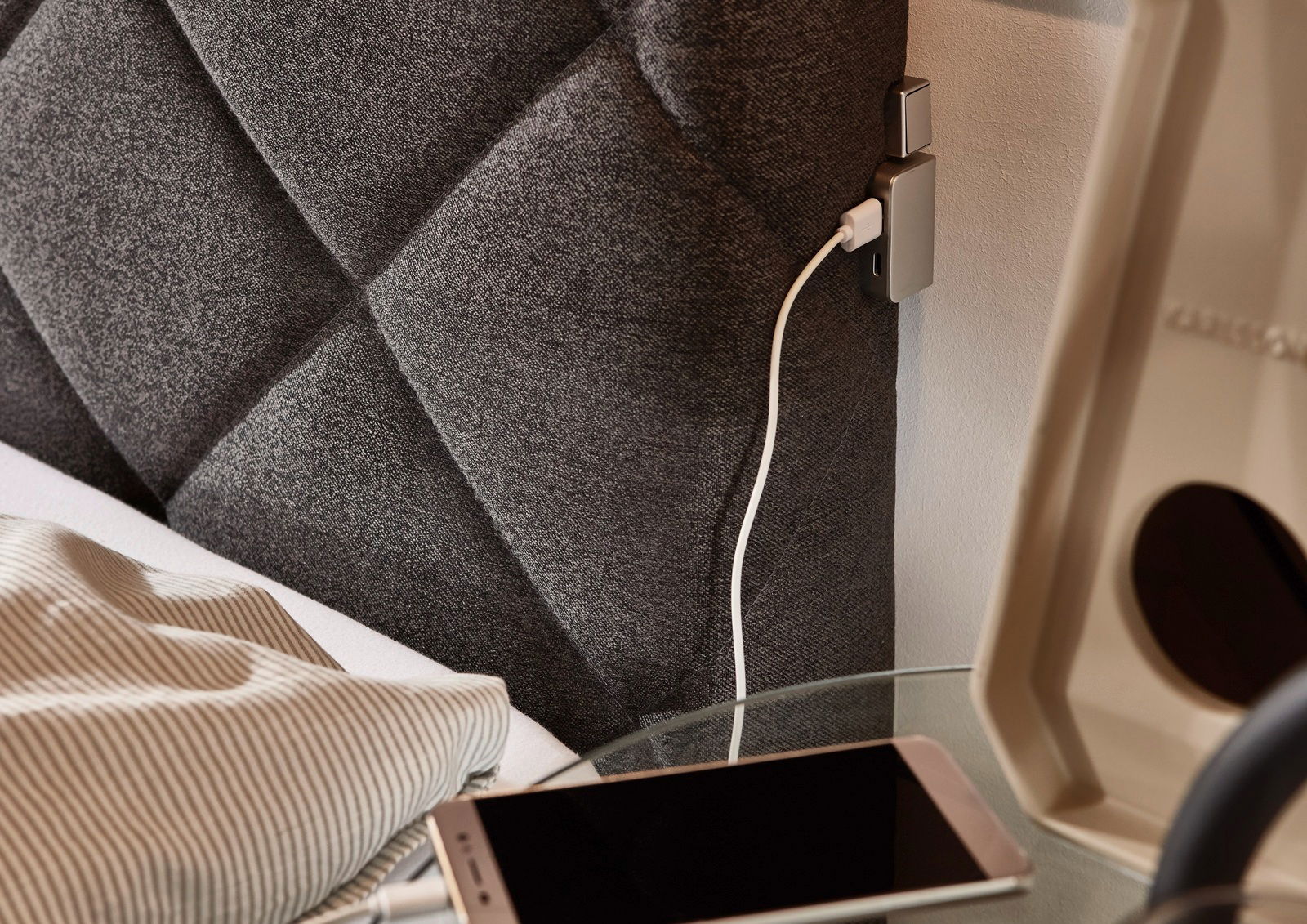 Nahaufnahme eines Boxspringbetts mit grauem, gestepptem Kopfteil und integriertem USB-Ladeanschluss, seitliche Perspektive.