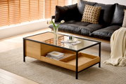 Moderner Couchtisch aus Holz und Glas mit schwarzem Metallrahmen, seitliche Perspektive, dekoriert mit einer Vase und einer Tasse auf einem Teppich vor einem Sofa.