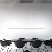 Moderne Pendelleuchte PURE Surface in minimalistischem Design, von der Seite betrachtet, über einem Esstisch mit schwarzen Stühlen.