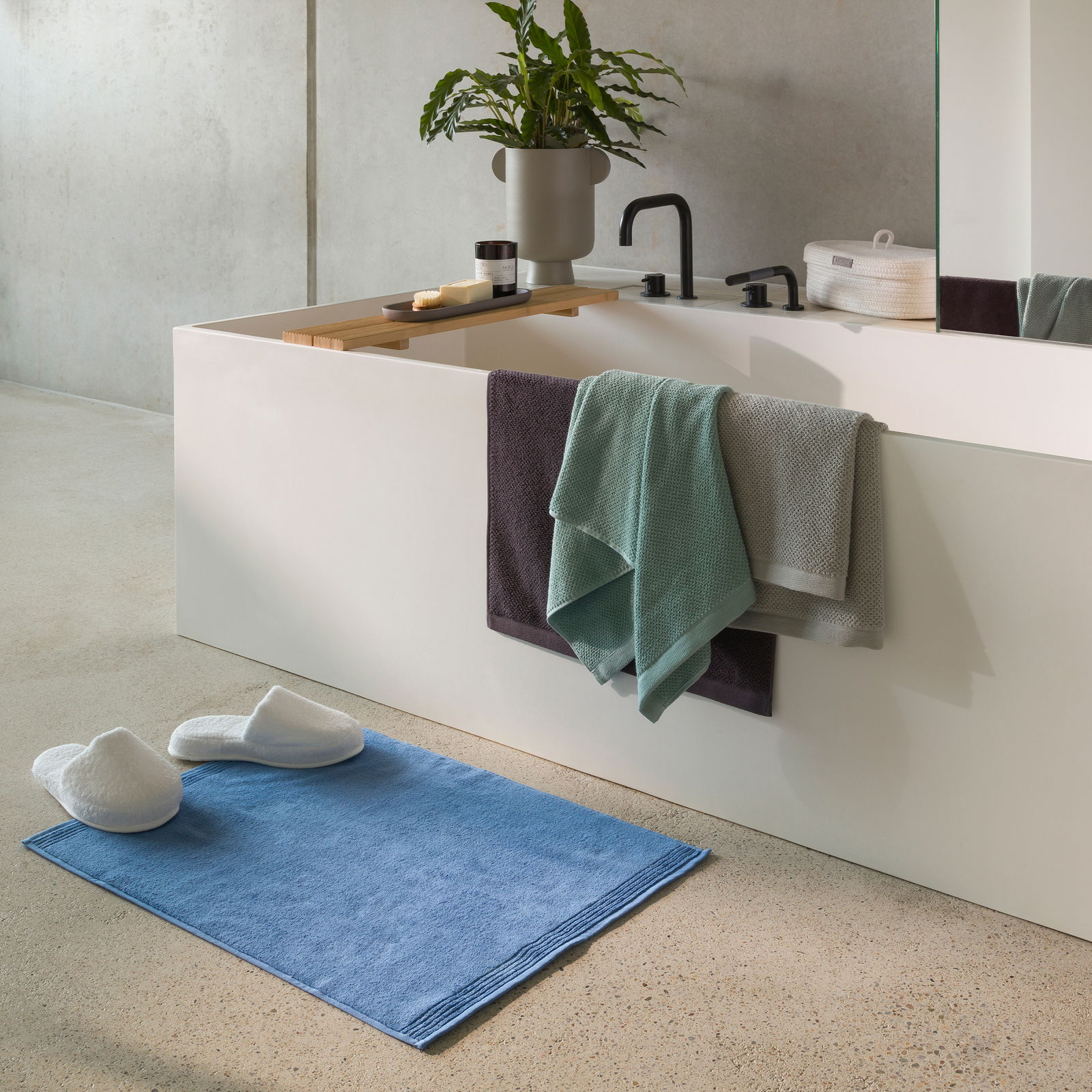 Badezimmer mit modernen Armaturen, Handtüchern in verschiedenen Farben und einem blauen Badteppich, seitliche Perspektive