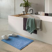 Badezimmer mit modernen Armaturen, Handtüchern in verschiedenen Farben und einem blauen Badteppich, seitliche Perspektive