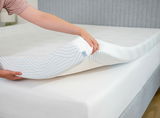 Eine Person hebt einen Tempur Topper Soft PRO PLUS SMARTCOOL an, um die weiche und flexible Struktur zu zeigen. Perspektive von der Seite des Bettes.