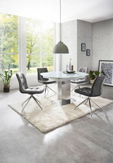 Moderner Essbereich mit rundem Glastisch und vier grauen Stühlen auf einem weißen Teppich, seitliche Perspektive.