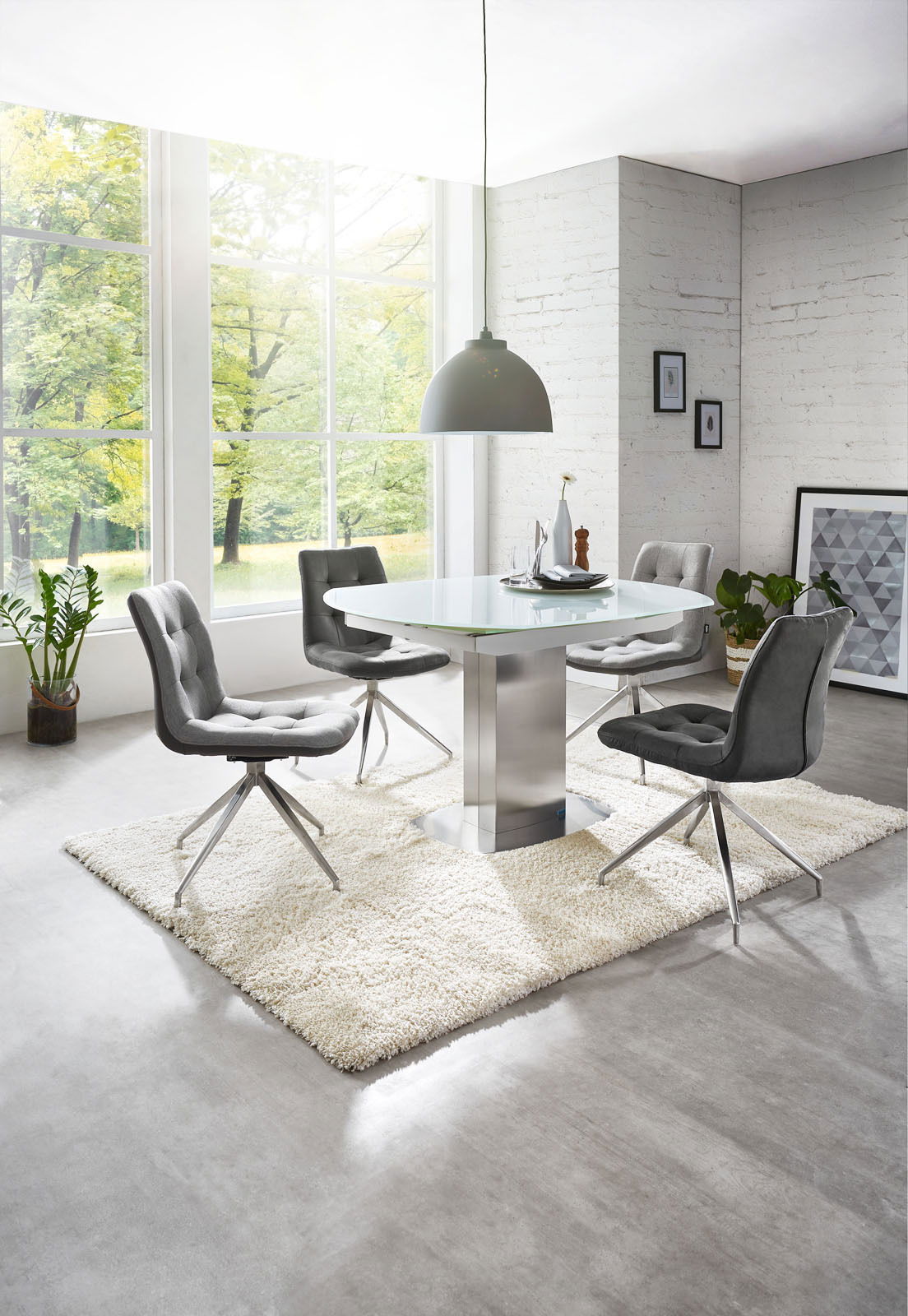 Moderner Essbereich mit rundem Glastisch und vier grauen Stühlen auf einem weißen Teppich, seitliche Perspektive.
