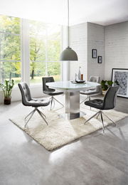 Moderner Essbereich mit rundem Glastisch und vier grauen Stühlen auf einem weißen Teppich, seitliche Perspektive.
