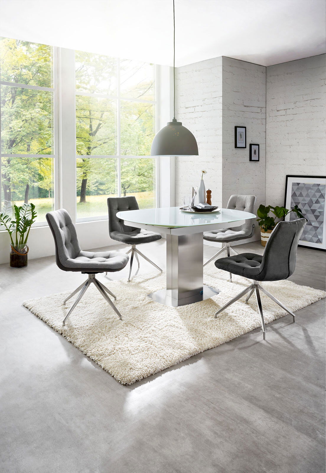 Moderner Essbereich mit rundem Glastisch und vier grauen Stühlen auf einem weißen Teppich, seitliche Perspektive.