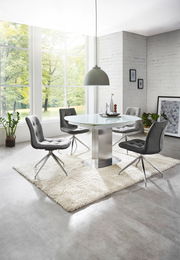 Moderner Essbereich mit rundem Glastisch und vier grauen Stühlen auf einem weißen Teppich, seitliche Perspektive.