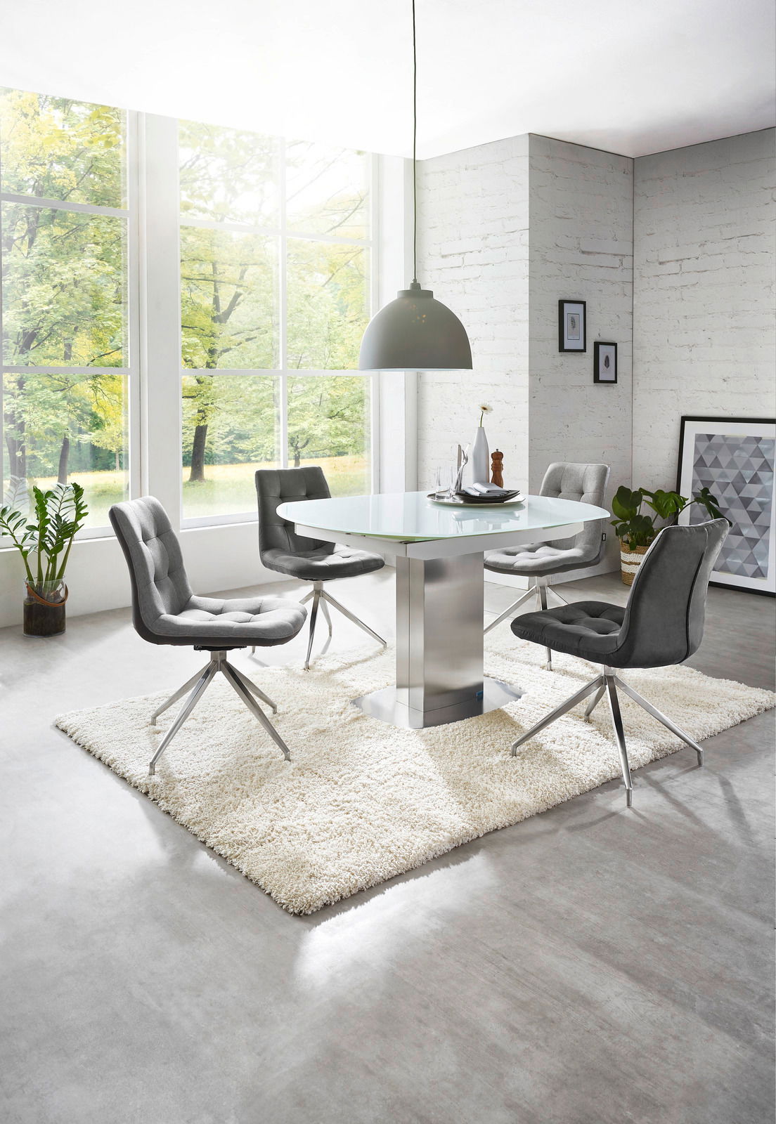 Moderner Essbereich mit rundem Glastisch und vier grauen Stühlen auf einem weißen Teppich, seitliche Perspektive.