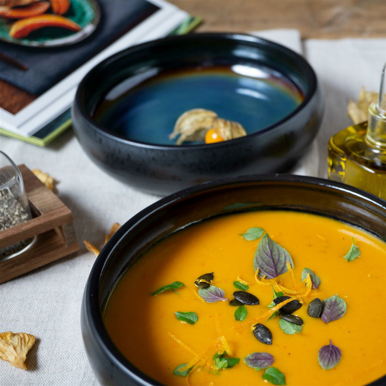 Zwei stilvolle Suppenteller in Blau-Braun, einer gefüllt mit Kürbissuppe, aus der Vogelperspektive fotografiert.