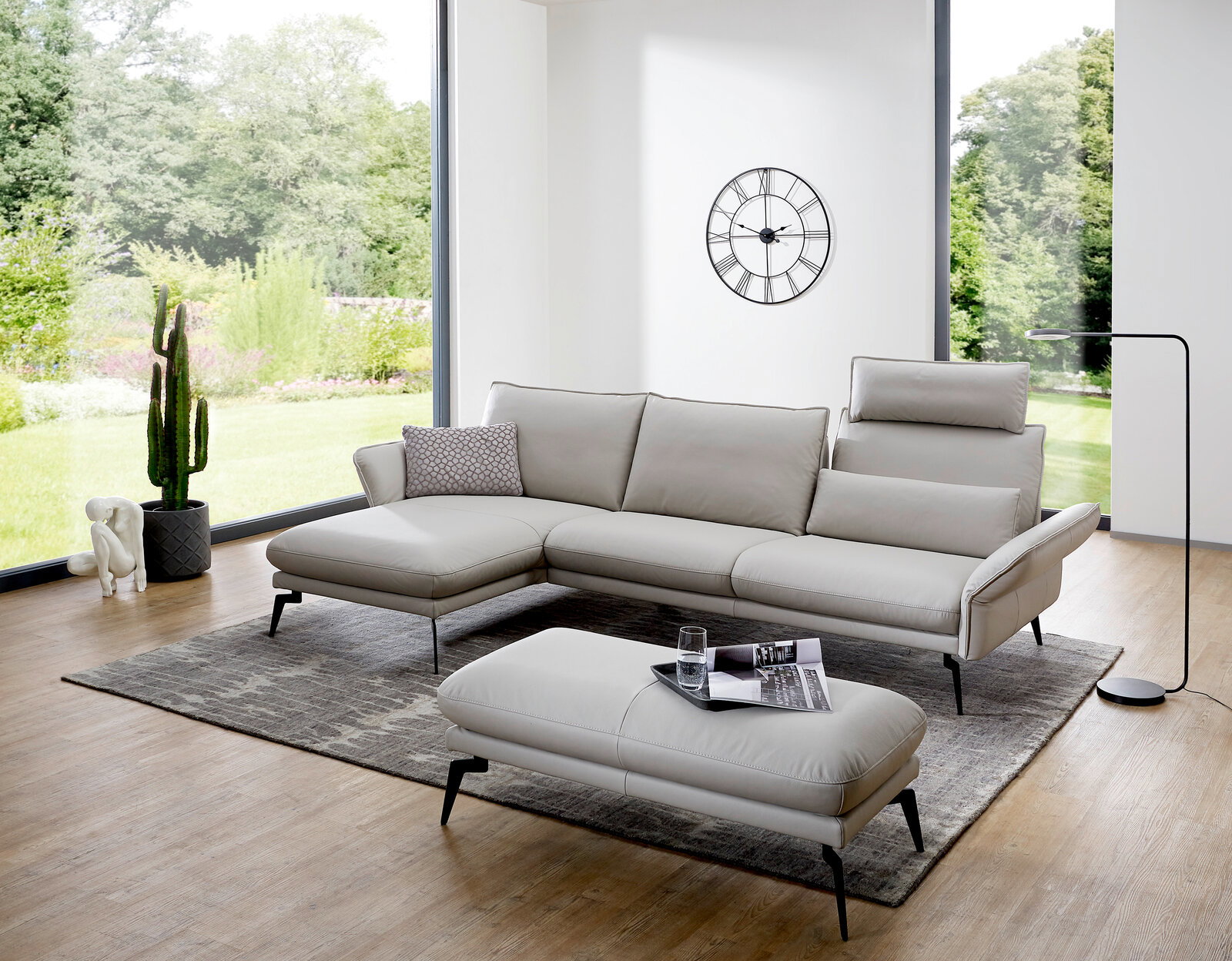 Moderne Hockerbank in einem hellen Wohnzimmer mit großen Fenstern, die einen Blick auf einen grünen Garten bieten. Perspektive von vorne.