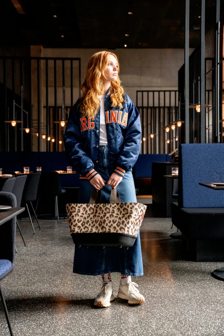 Een vrouw in een modern café houdt een boodschappentas met luipaardprint vast, vooraanzicht
