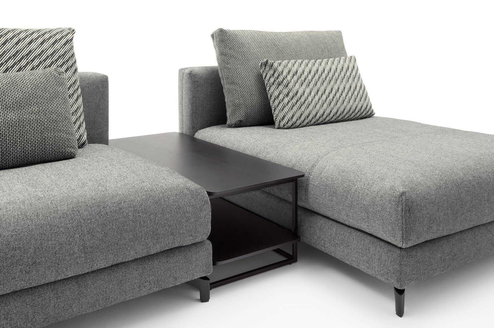 Moderner Anstelltisch in dunklem Holz zwischen zwei grauen Sofas, seitliche Perspektive.