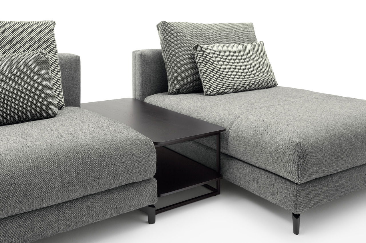 Moderner Anstelltisch in dunklem Holz zwischen zwei grauen Sofas, seitliche Perspektive.