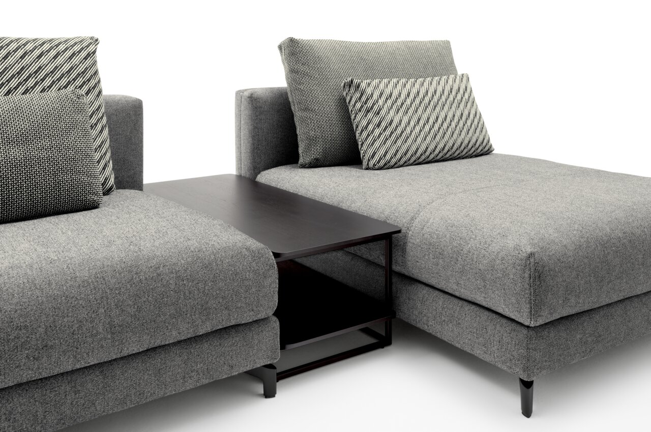 Rolf Benz Anstelltisch 987 Moderner Anstelltisch in dunklem Holz zwischen zwei grauen Sofas, seitliche Perspektive.